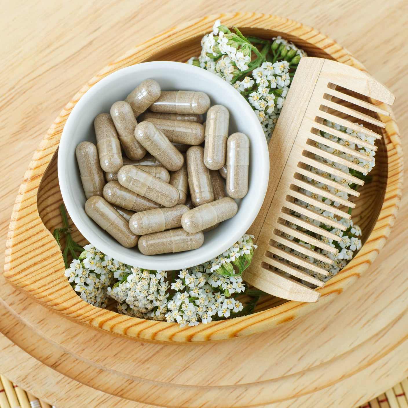 Hair growth supplement capsules in a wooden bowl with botanical ingredients and a wooden hair comb