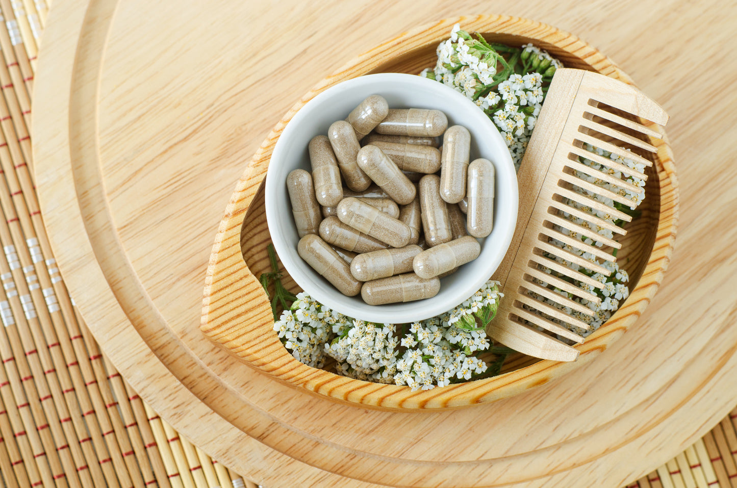 Hair growth supplement capsules in a wooden bowl with botanical ingredients and a wooden hair comb